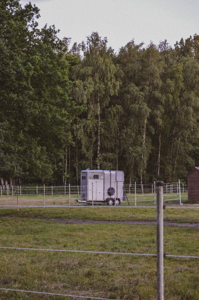 A tranquil farm scene featuring a horse trailer amidst lush greenery, perfect for rustic themes.